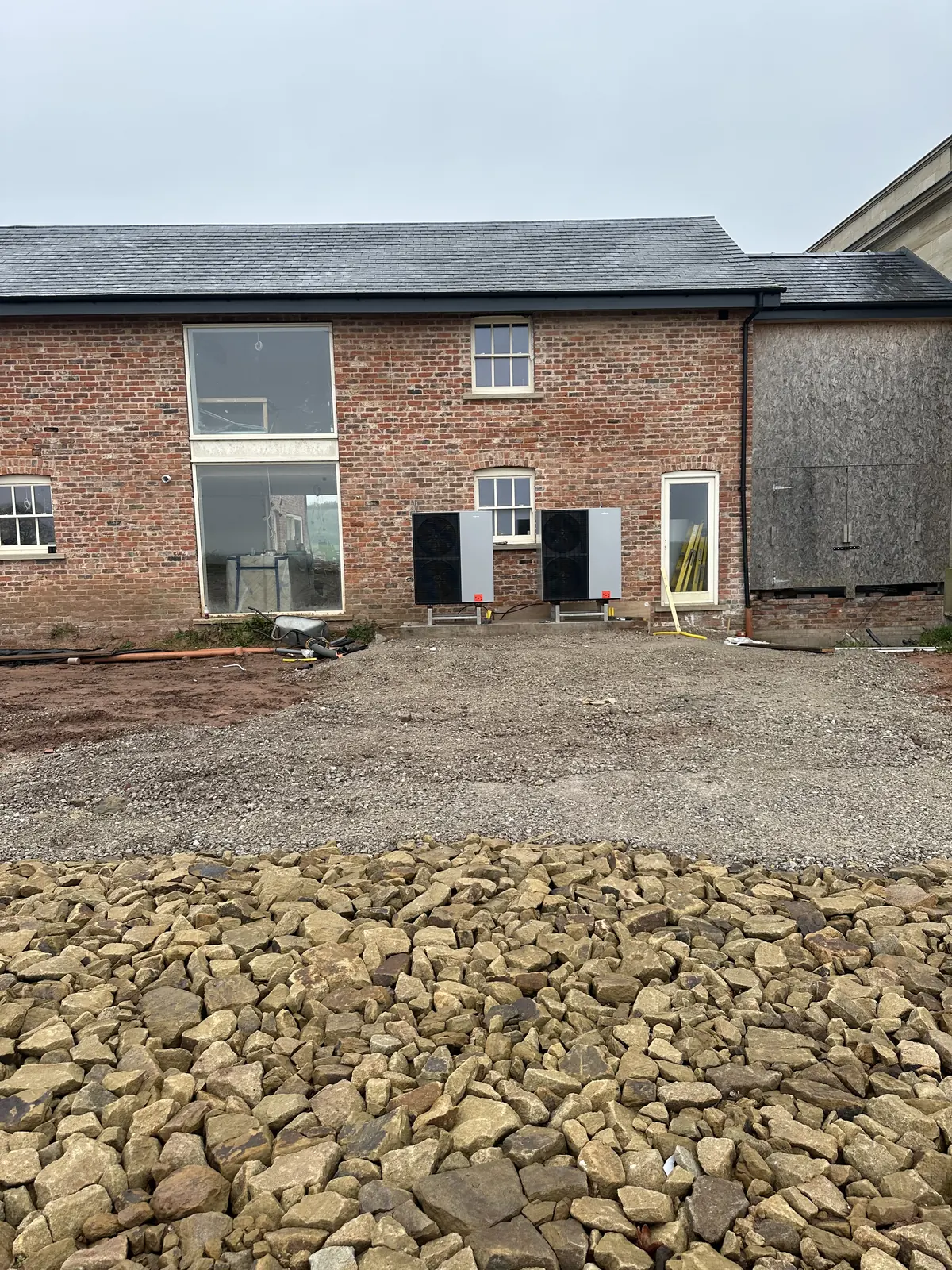 Wider view of two air source heat pumps beside a brick building