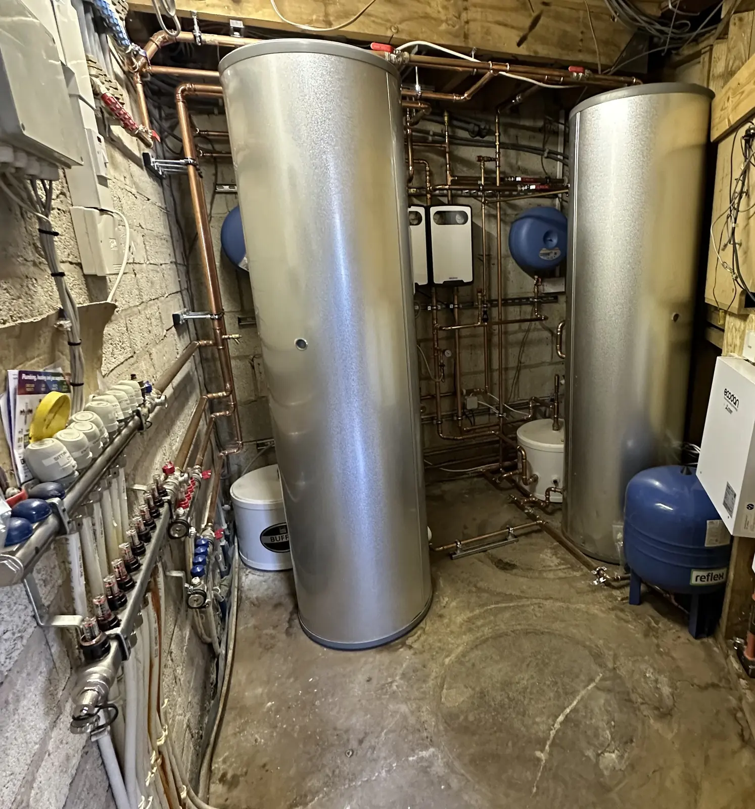 Plant room with two hot water cylinders, heat pump controllers and underfloor heating manifolds